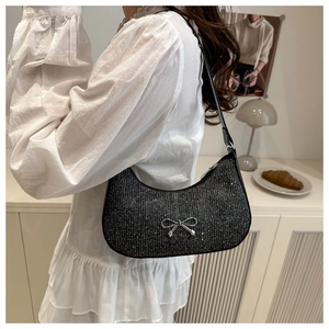 Detail shot of a black glitter crescent bag with a silver metal bow and leather strap