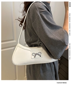 Detail of white leather baguette bag featuring a metallic silver bow buckle and stitching