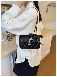 Close-up of black quilted shoulder bag with gold hardware and silk scarf detail