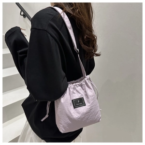 Detail of light purple drawstring bucket bag featuring a black brand logo and woven strap