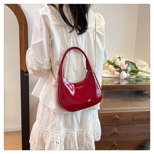 Detail of red patent leather crescent bag featuring gold chain and glossy hobo texture