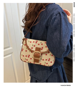 Détail du sac bandoulière imprimé cerises avec garniture en cuir brun et boucle dorée