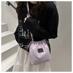 Close-up of a lavender nylon drawstring bucket bag with a black logo patch and adjustable strap