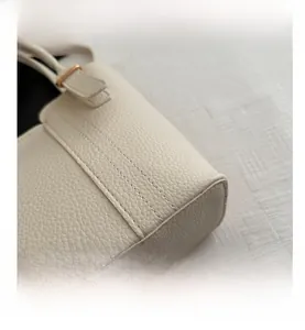 Close-up of beige lychee leather stitching and golden metal buckle on bucket bag