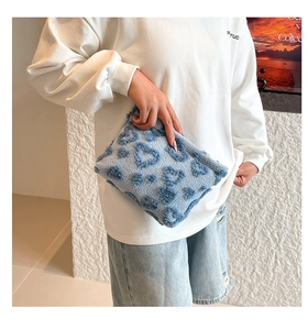 Detail view of a soft blue plush cosmetic bag with heart pattern held by a model.