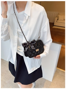 Close-up of black quilted shoulder bag featuring metal chain and silk scarf bow detail