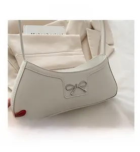 Close-up of cream leather crescent bag with silver bow buckle on a beige blazer