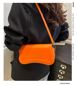 Detail view of orange leather crossbody bag with curved bottom and gold hardware