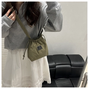Detail of army green nylon drawstring bucket bag with black logo patch and wide strap
