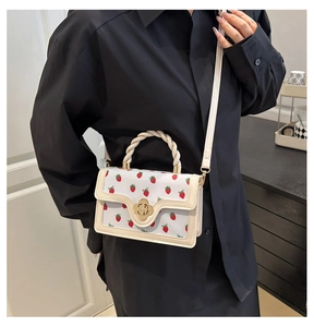 Close-up of a white strawberry pattern handbag with a braided handle worn by a model