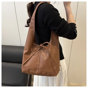 Seitenansicht einer braunen Ölwachs-Ledertasche mit eleganter Schleifendekoration.