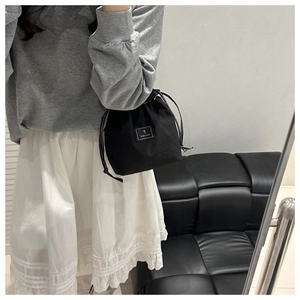 Detail of a black nylon drawstring bucket bag with a white square logo patch for women