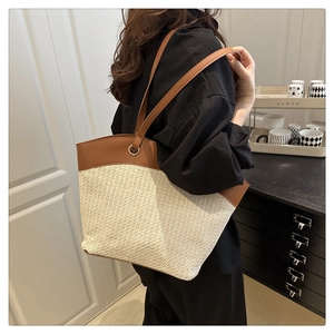 Detail of cream woven tote bag with brown leather trim and handles shown on a model