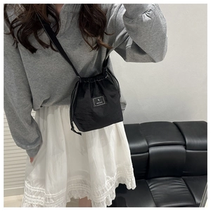 Close-up of black drawstring bucket bag featuring white logo patch and adjustable strap
