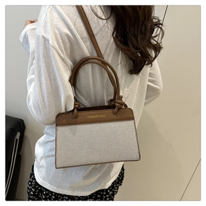 Detail of a chic cream canvas handbag with brown leather trim and golden logo