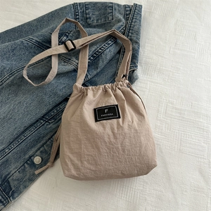 Detail of light beige drawstring bucket bag with black brand label and adjustable strap
