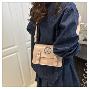 Detail of beige leather crossbody bag featuring silver M logo and dual decorative straps