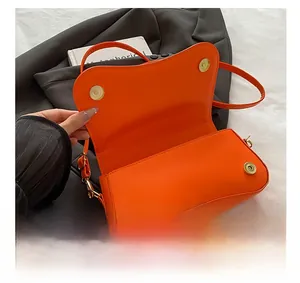 Detail view of orange leather handbag with gold magnetic clasps and sleek flap design