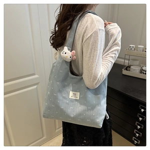 Detail of light blue corduroy tote bag with bow prints and plush kitty charm
