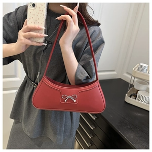 Detail of red leather shoulder bag featuring a polished silver metal bow ornament