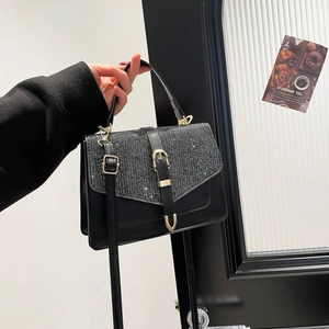 Elegant black crossbody bag with sequined flap and gold hardware held by hand