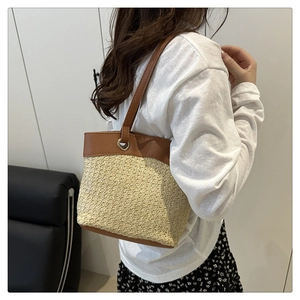 Detailed view of woven straw shoulder bag with brown leather trim worn by a model