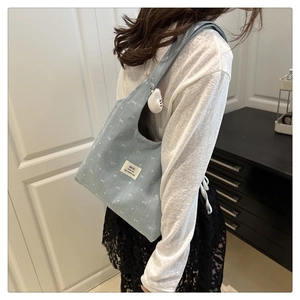 Detail of light blue canvas tote bag with bow prints and a white cat plush keychain