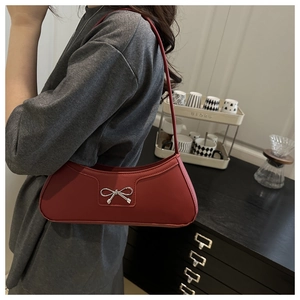 Red shoulder bag with silver bow detail worn by a model in a modern interior setting