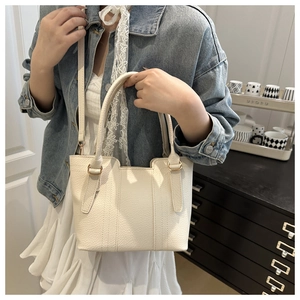 Close-up detail of white pebble leather tote bag with gold hardware and stitch accents