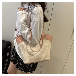 Detail of a large woven straw tote bag with pink leather trim worn by a model