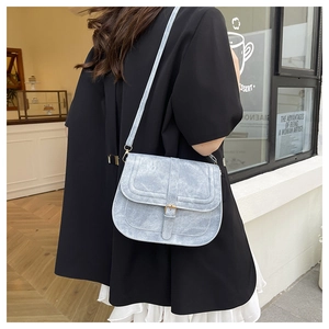 Light blue saddle bag with textured finish shown on model in a cafe setting