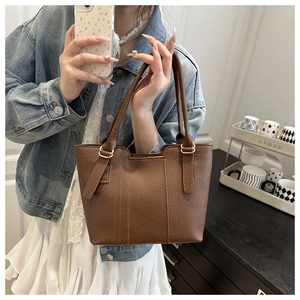 Detail showing the brown lychee pattern leather texture and metal handle buckle of the tote