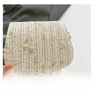 Detailed embroidery of light green and yellow flowers on a woven straw saddle bag