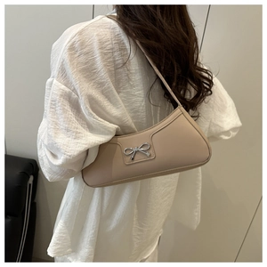 Detail of beige baguette bag with silver bow buckle worn over a white textured shirt