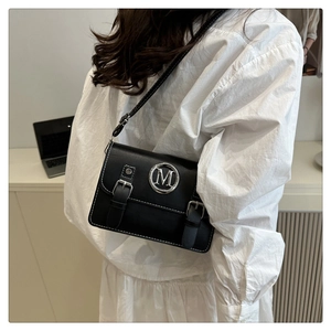 Detail of black leather crossbody bag with white stitching and silver M logo on a model
