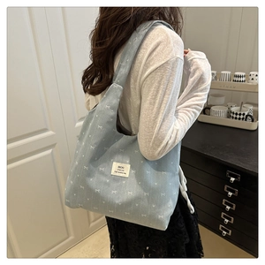 Detailed view of light blue denim tote bag featuring white bow prints and rectangular label