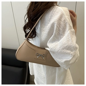 Detail of beige crescent underarm bag featuring a delicate silver metal bow accessory