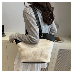 Detail of hand-woven straw tote with black leather straps and gold metal eyelets on model