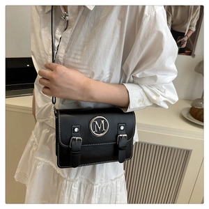 Detail of a black crossbody bag with silver M logo and white contrast stitching detail