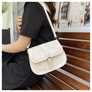 Close-up of ivory velvet saddle bag showing fine texture and leather strap on a wooden bench