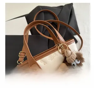 Detail of cream and brown bucket bag featuring embossed patterns and a plush monster charm