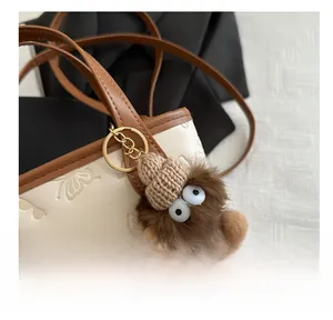 Close-up of a brown plush monster charm with knit hat on a textured white bucket bag
