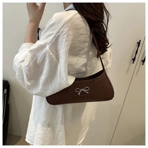 Close-up of brown leather bag with silver bow charm worn by a model in white