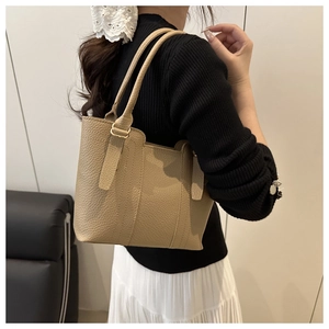 Close-up of beige leather tote bag with lychee texture worn over the shoulder by a model