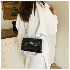 Détail du sac noir à texture crocodile avec bandoulière chaîne argentée sur blanc