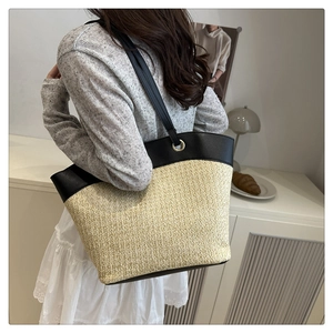 Detail of summer tote bag featuring straw weave texture and black leather shoulder straps