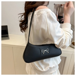 Close-up of matte black underarm bag with a silver bow accent shown on a model