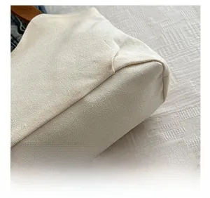 Close-up of reinforced stitching on minimalist white canvas tote bag with brown handles