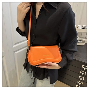 Detail view of bright orange leather shoulder bag with adjustable strap on a black shirt