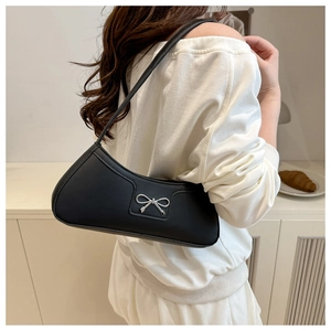 Detail of a black matte leather underarm bag with a silver metallic bow ornament on a woman